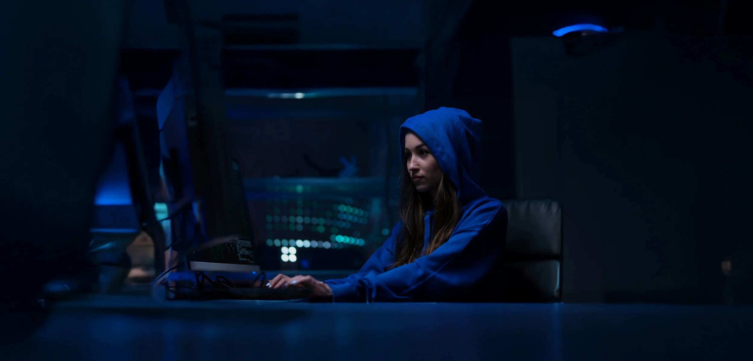 Woman hacker in a dark room working on a laptop, illustrating cybersecurity threats faced by Fortune 500 companies
